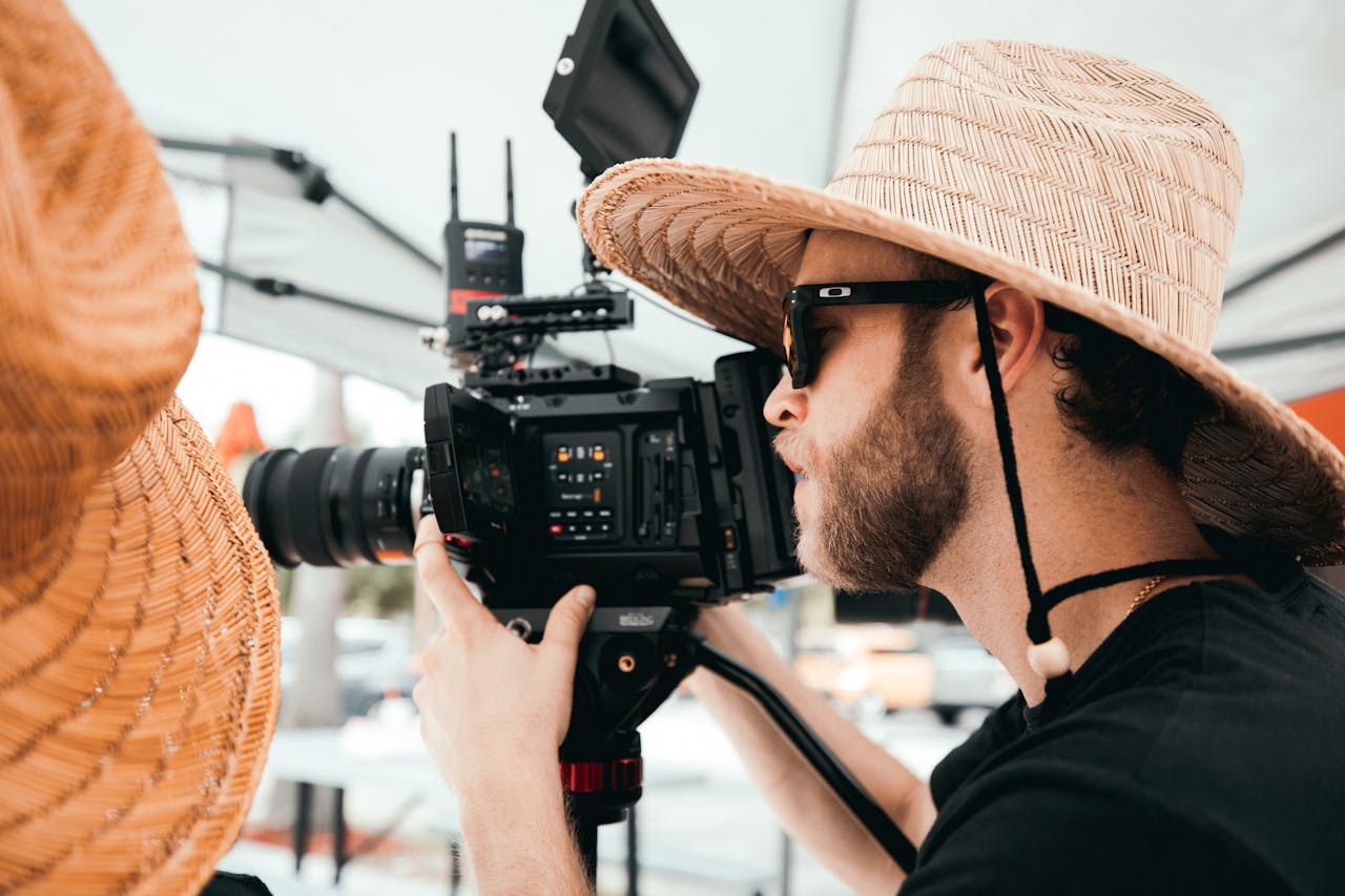 creative-03 A bearded man with glasses operates a professional video camera during an outdoor shoot.