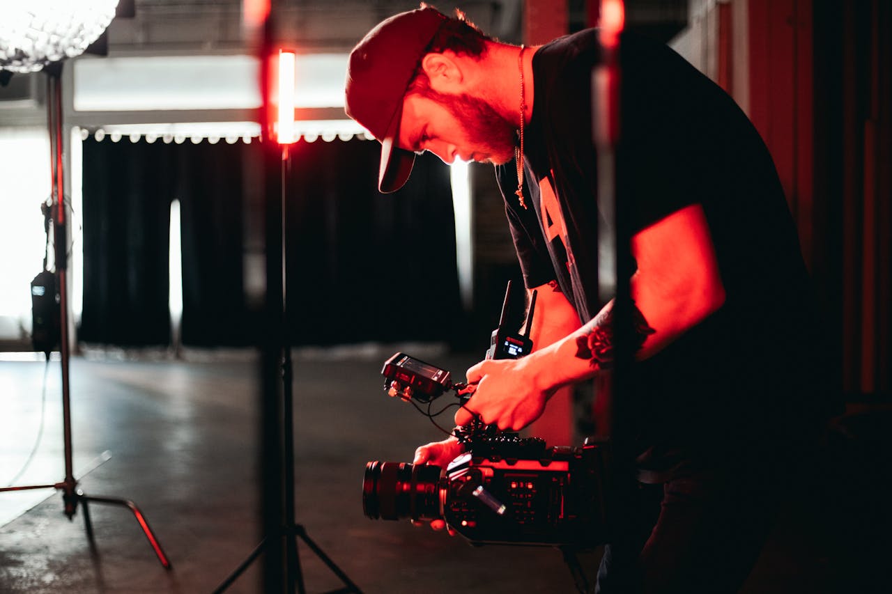 mobile-01 Male videographer adjusting camera equipment in an indoor studio setting with dim lighting.