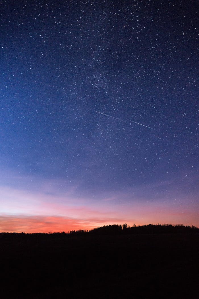 Services-02 A breathtaking view of a starry night sky with a shooting star over Lithuania's landscape at sunset.