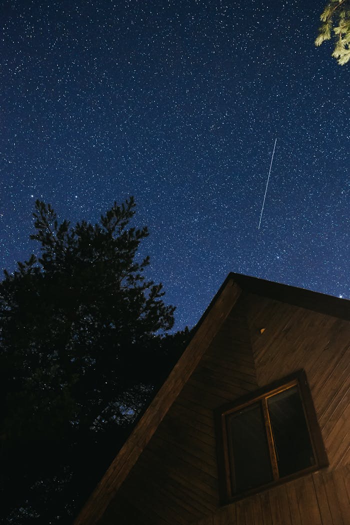 creative Clear night sky filled with stars and a shooting star above a wooden cabin.